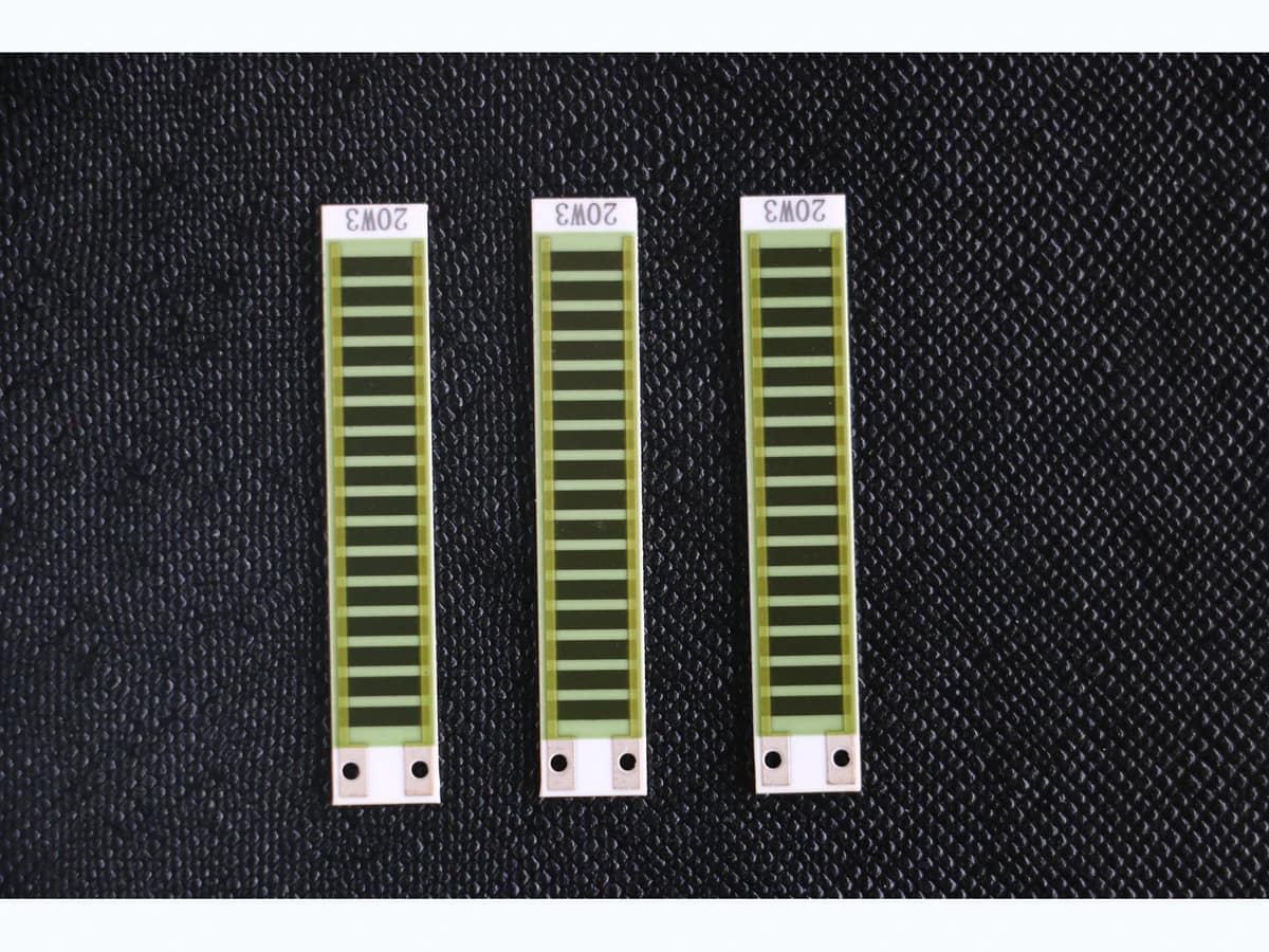 Three long ceramic thick film resistor network strips with repeated printed elements and value labels on a clean black surface