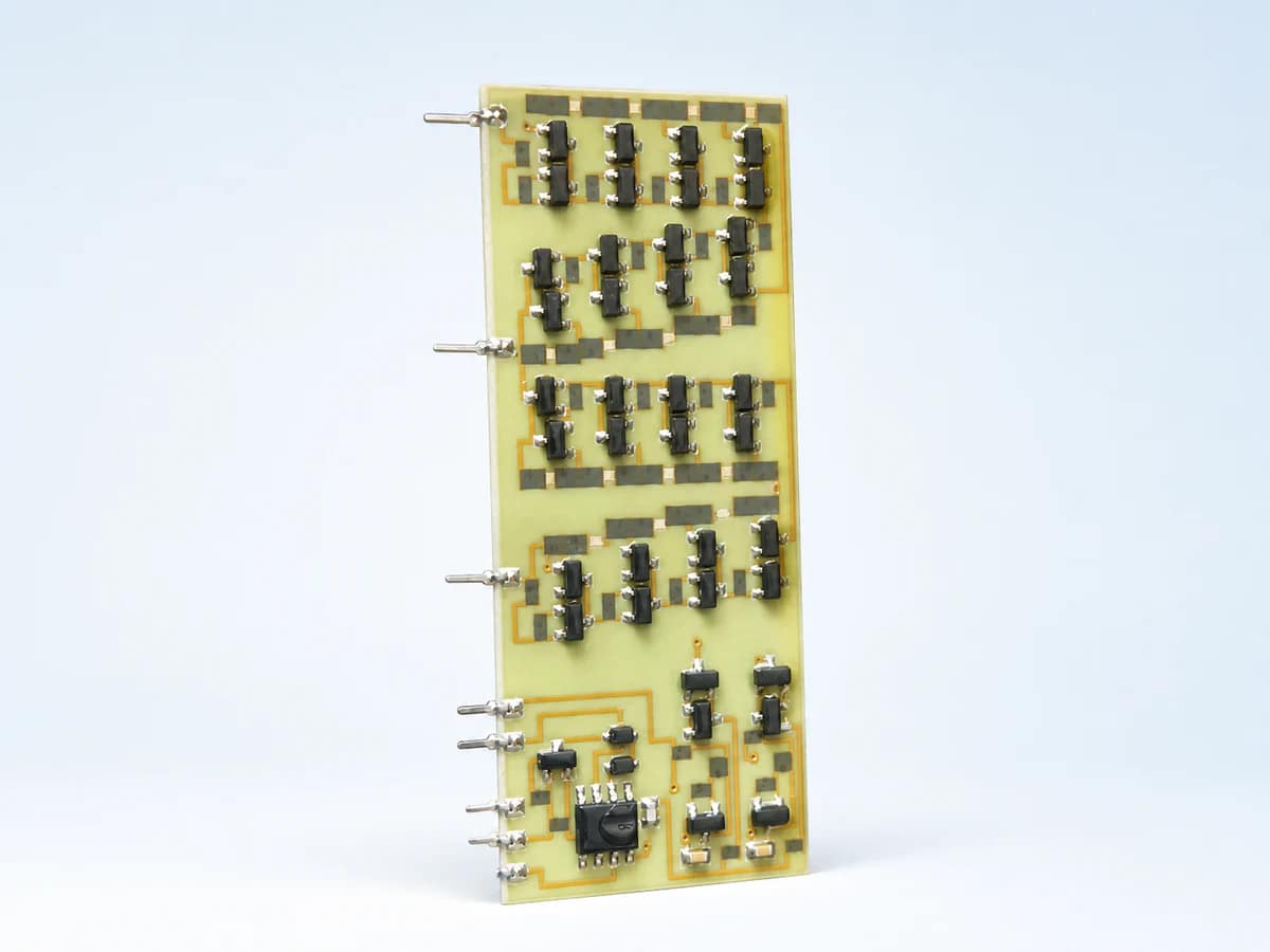 Clean studio view of a real pale-green rectangular ceramic circuit populated with black components, silver solder joints, gold conductor paths, and side terminals