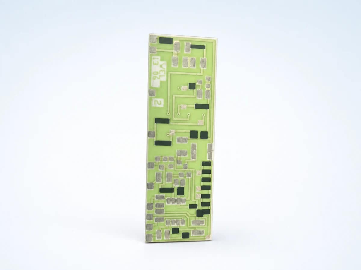 Studio product view of a pale-green ceramic circuit with silver pads, dark printed features, and visible surface routing