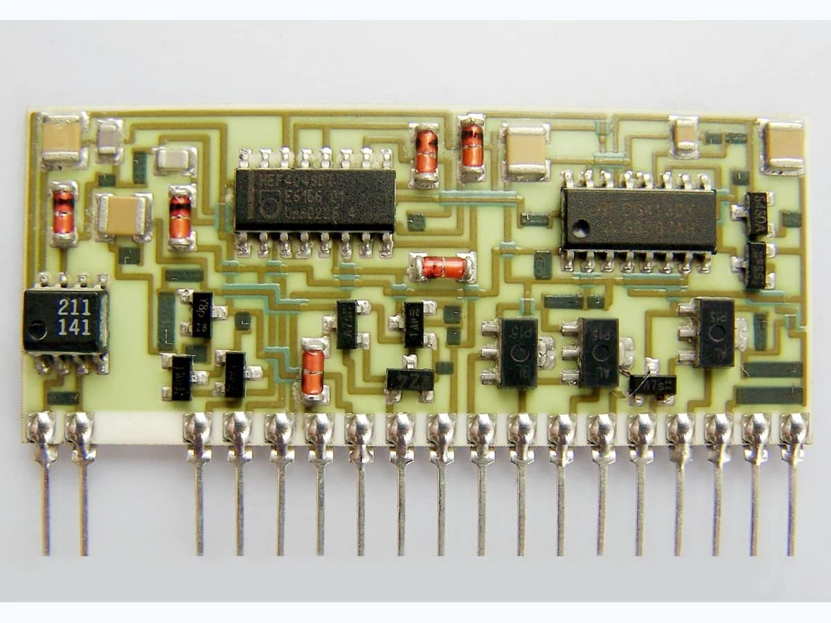 Supplied thick film hybrid circuit photograph showing printed routing, mounted components, and a row of metal leads