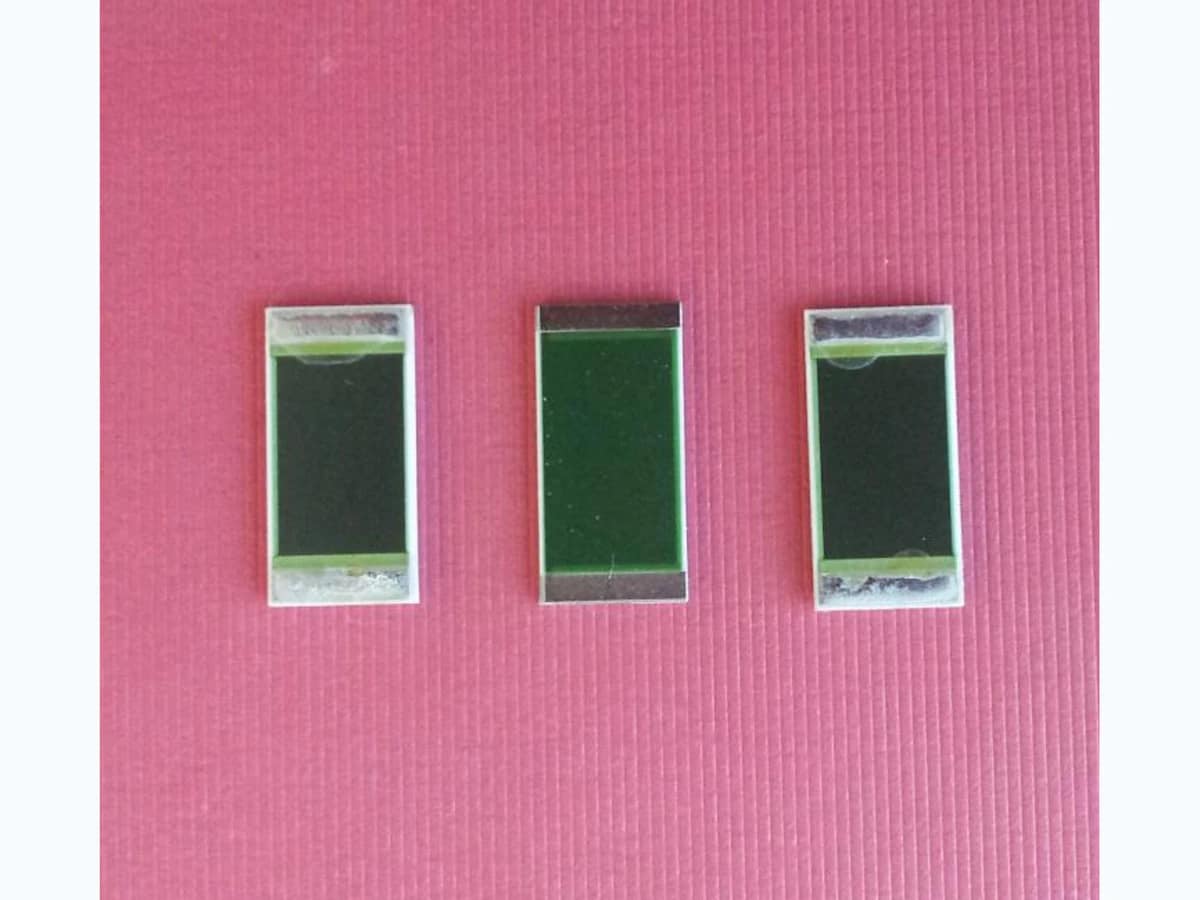 Three rectangular thick film power resistors with broad dark resistor films and silver-colored end terminals on a clean pink surface