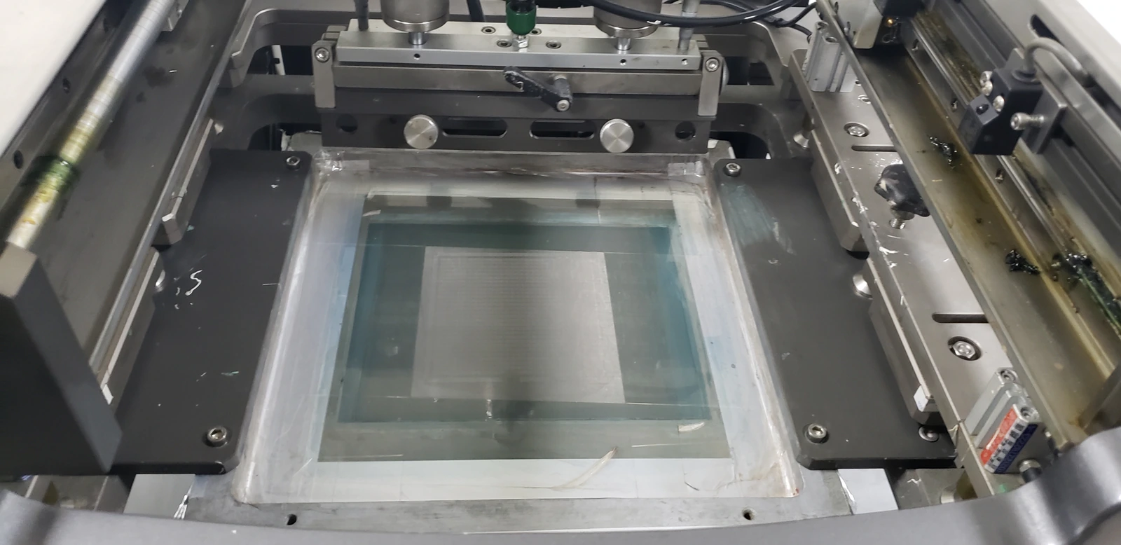 A screen frame, print bed and registration fixture: wet deposit volume is tied to the actual patterned area.