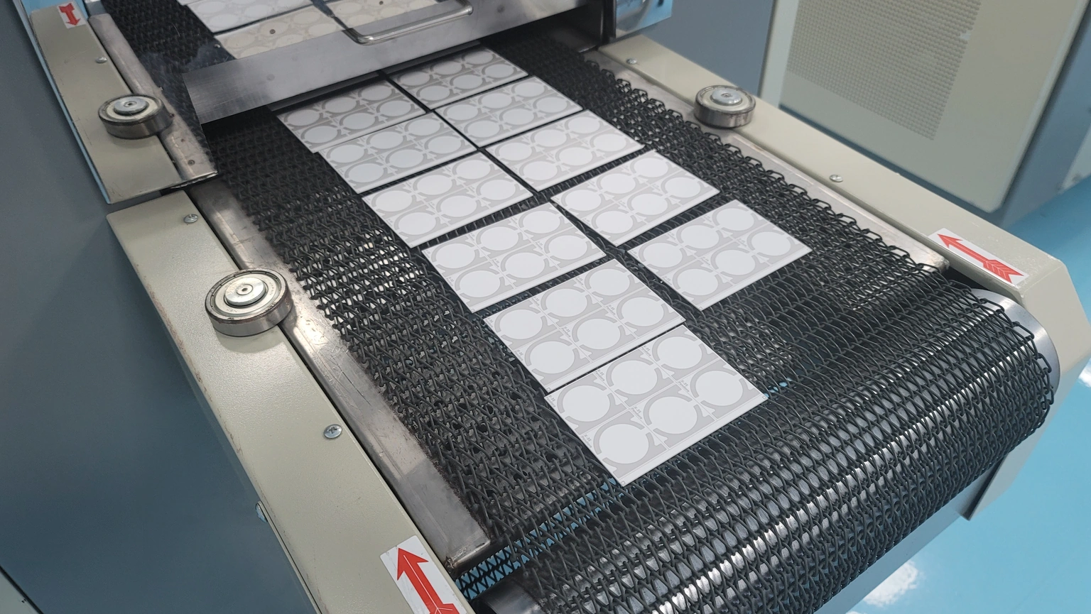 Printed ceramic panels arranged on a mesh conveyor belt at a thermal-process opening.