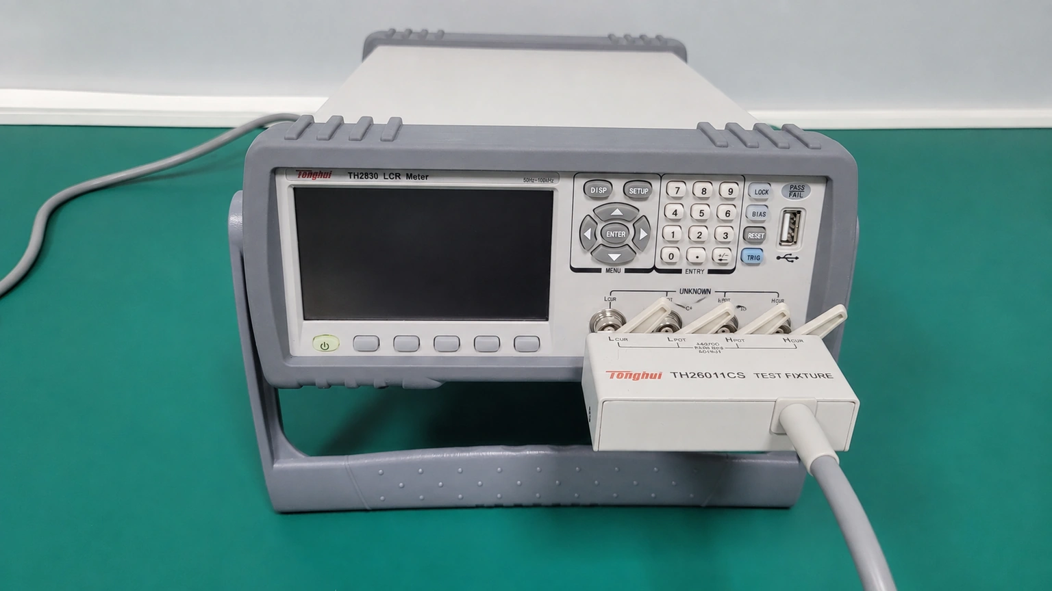 An LCR meter with an inactive screen and a connected open test fixture before specimen installation.