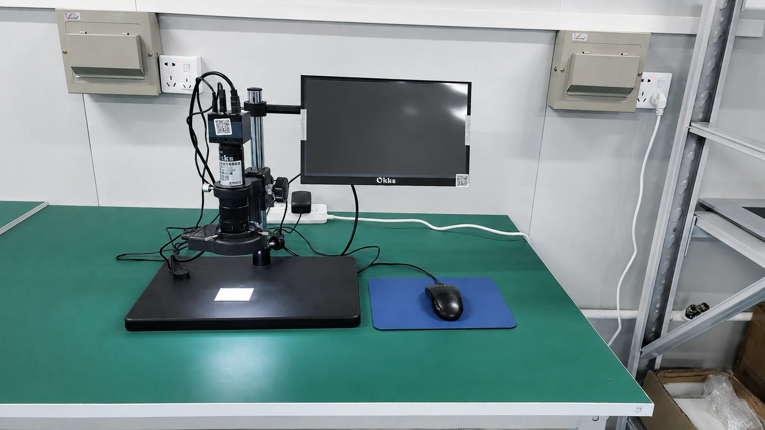 A bench-mounted inspection camera and objective above a plain witness slide, beside an inactive monitor.