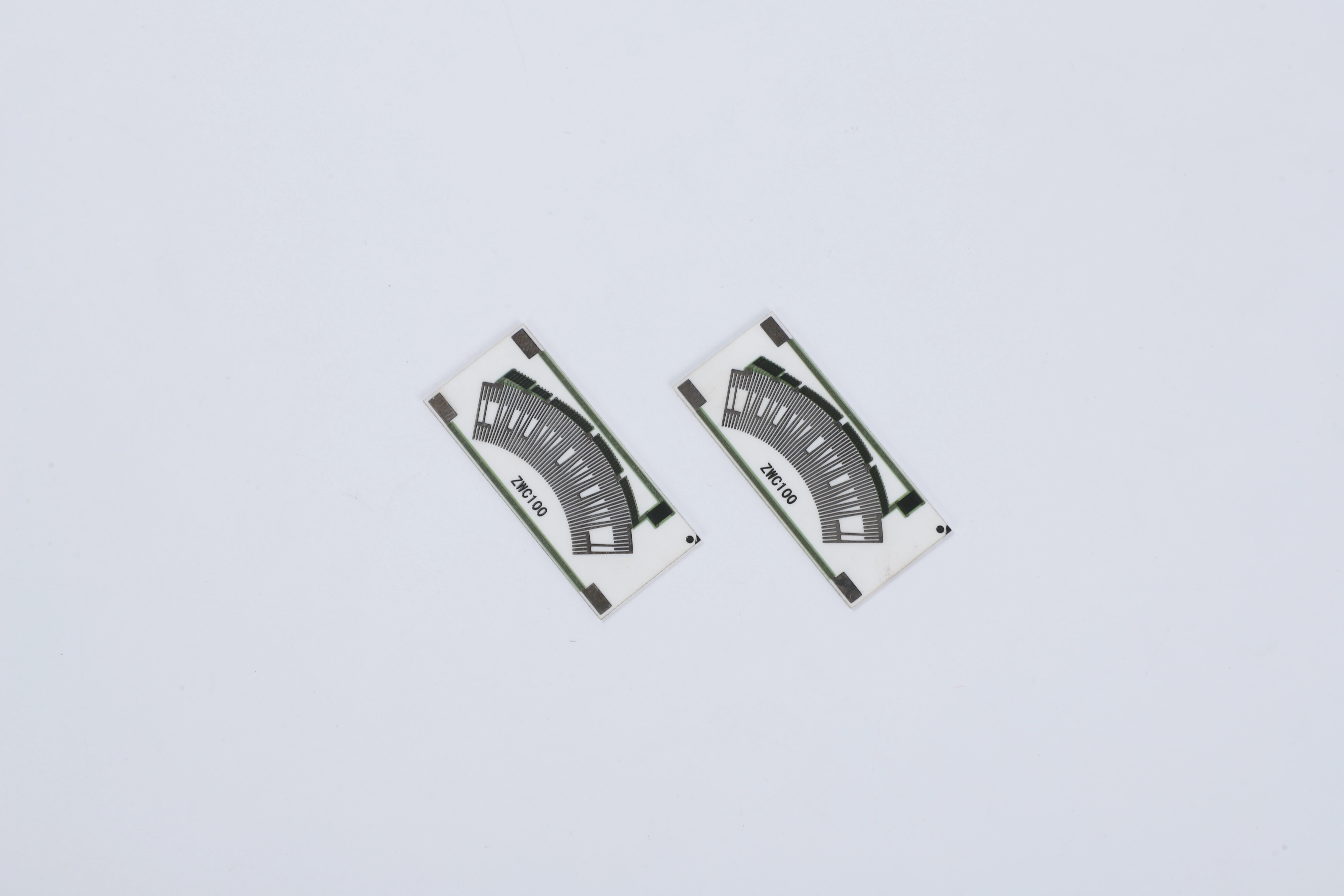 Two rectangular ceramic contact cards with curved segmented tracks, terminal pads and corner holes.