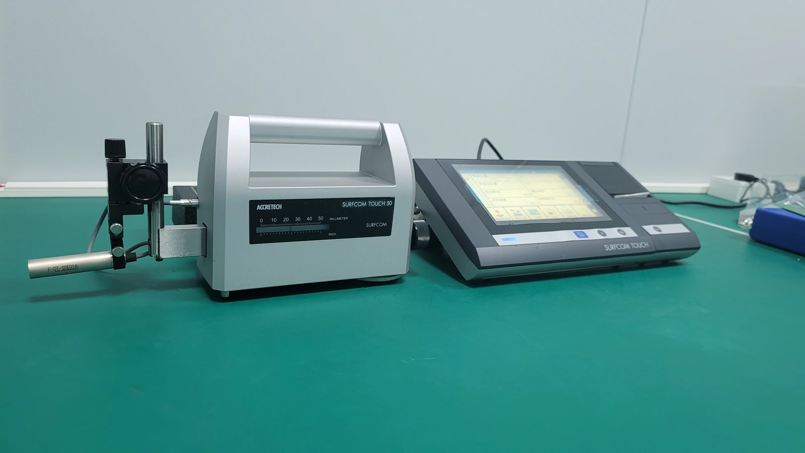 A surface profilometer with its stylus pickup, traverse body and touchscreen controller visible together.