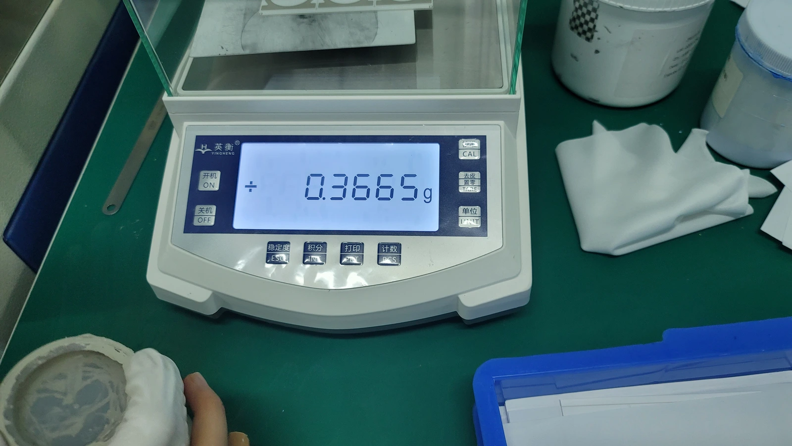 A laboratory balance with a sample container and handling accessories on the adjacent bench.