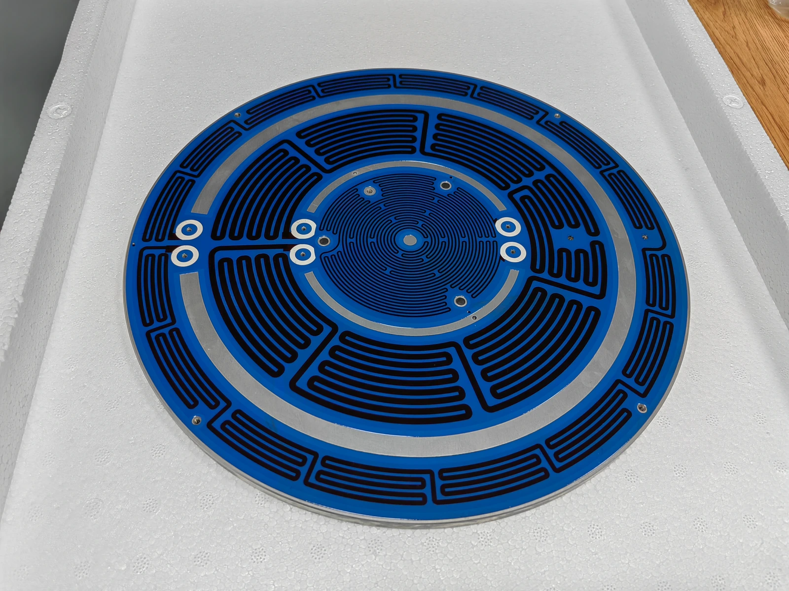 A blue-coated circular heater plate with several routed heating regions and exposed connection holes.