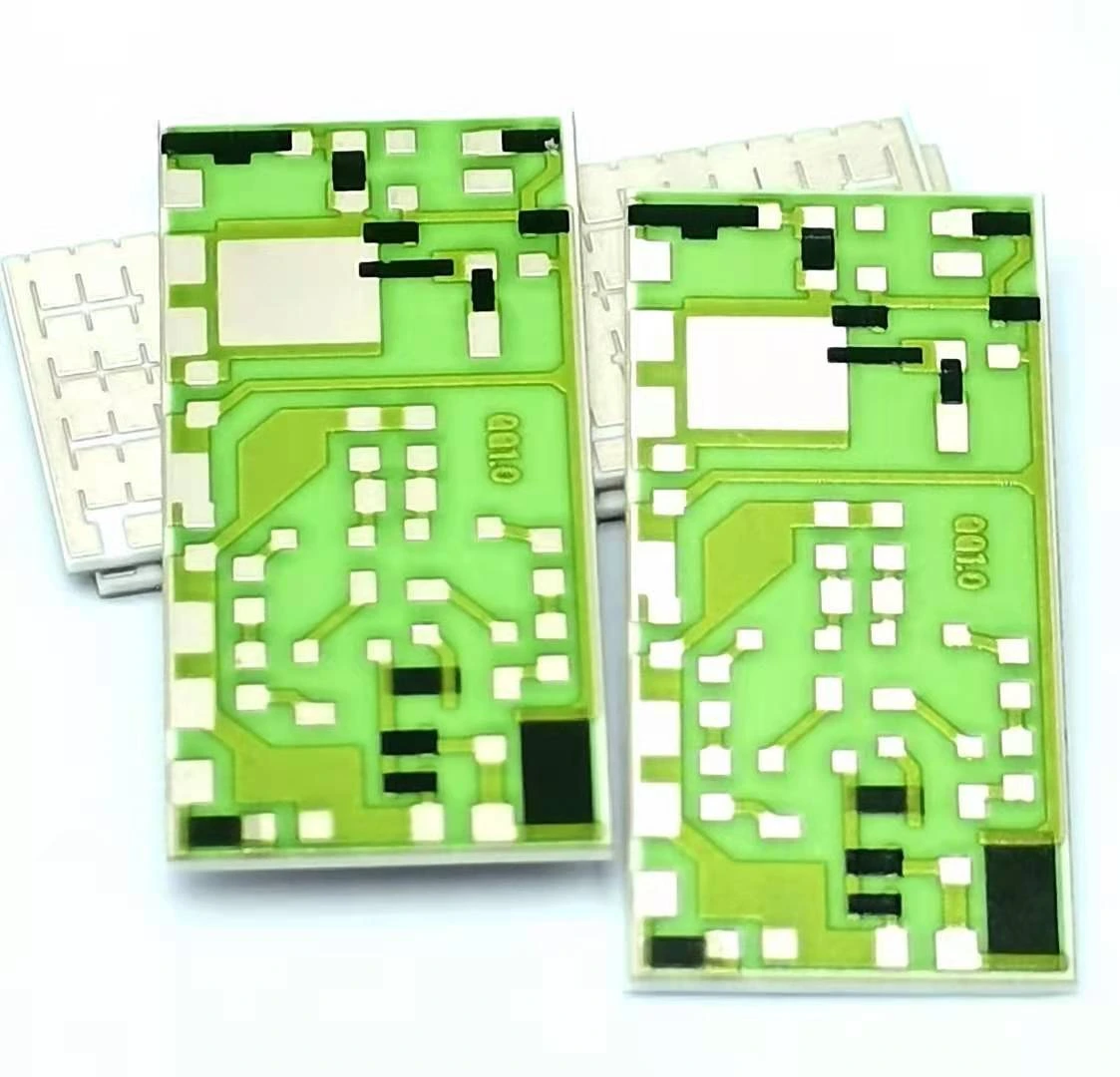 Two green-glazed ceramic circuit parts with fine conductor routing, black resistor regions and large exposed pads.