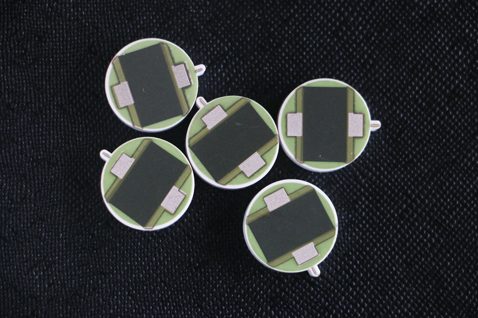 Circular ceramic resistor elements with broad grey resistive regions, green protection and exposed side terminals.