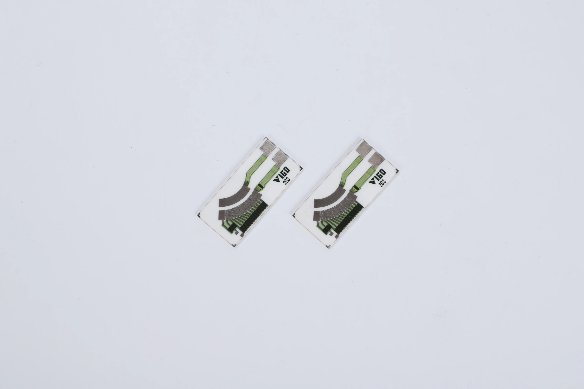 A pair of narrow ceramic contact cards with curved tracks and exposed terminal regions.