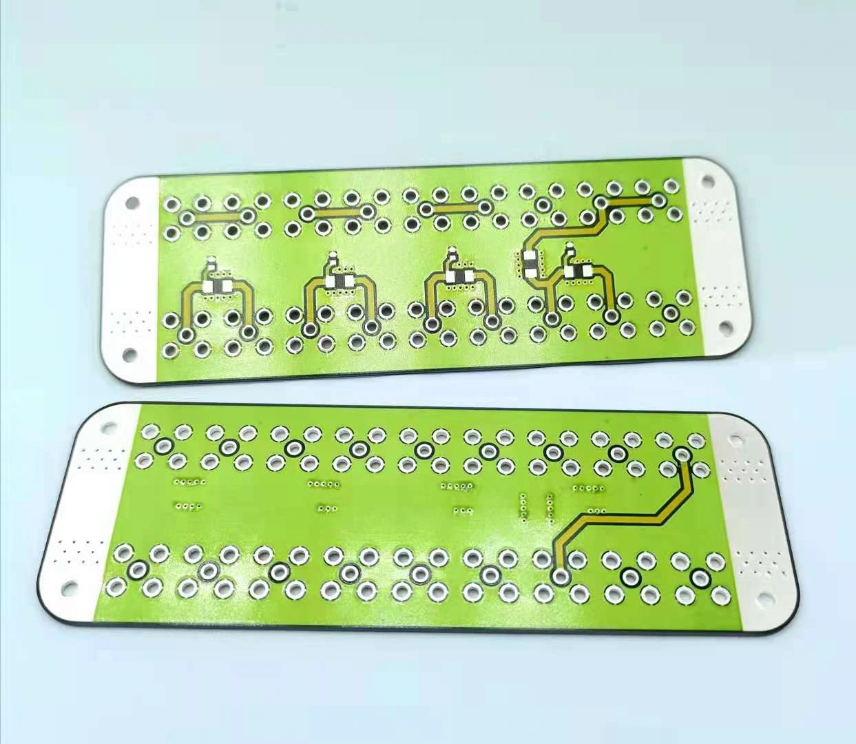 Two faces of an elongated ceramic circuit showing green protective coverage and many exposed connection holes.
