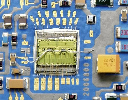 An exposed semiconductor die with fine bond wires connecting it to surrounding pads and electronic components.