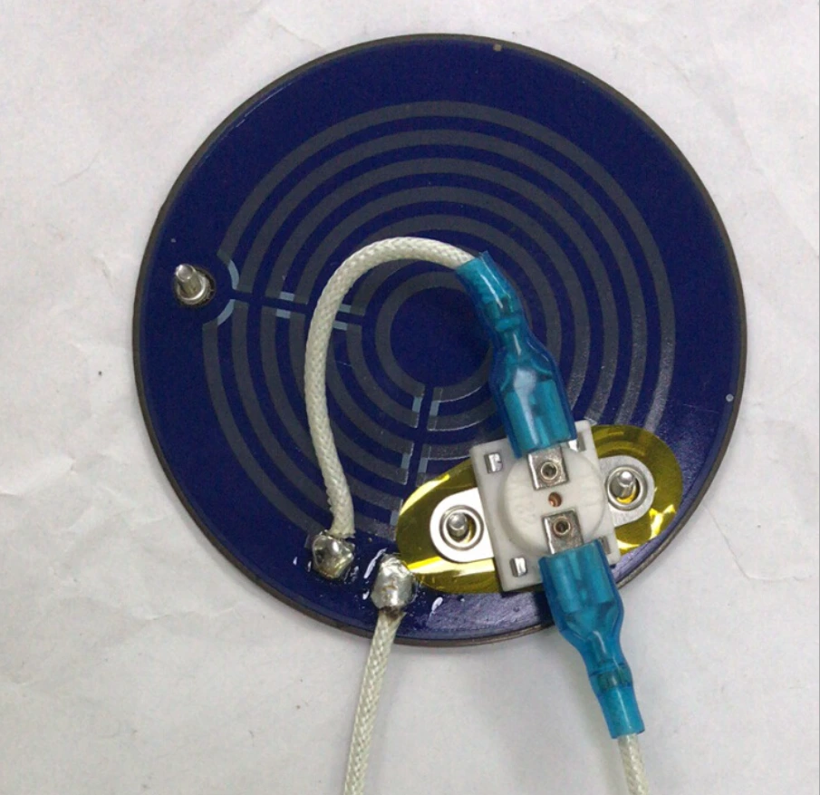 A circular heater assembly with attached leads and a metal-bodied temperature cutout.