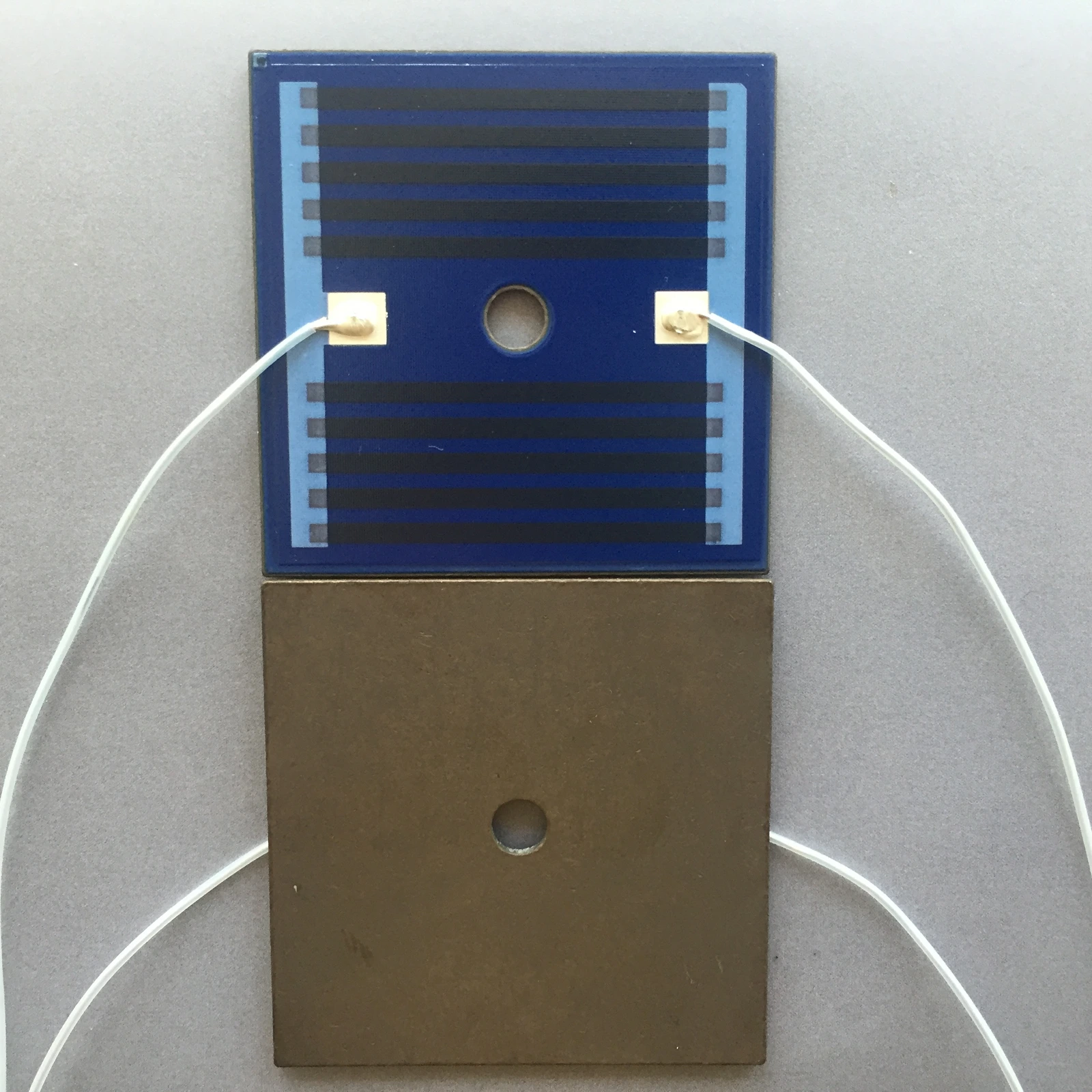 A blue-coated square heater plate positioned above a metal plate, both with central circular openings.