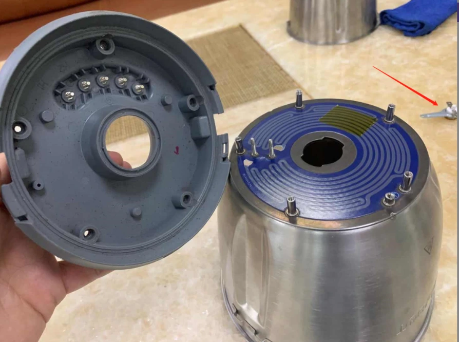 A circular heater plate beside an opened metal vessel interface, with perimeter fastening positions visible.