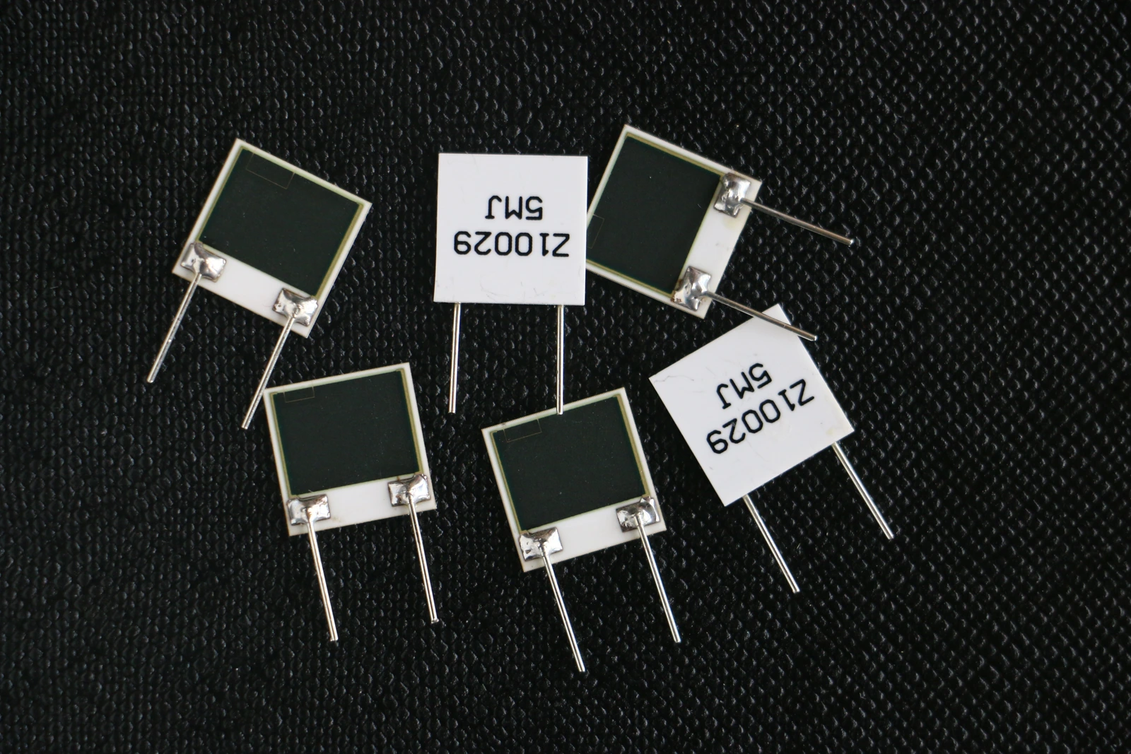 Rectangular resistor elements with dark film surfaces, ceramic edges and attached metal leads.