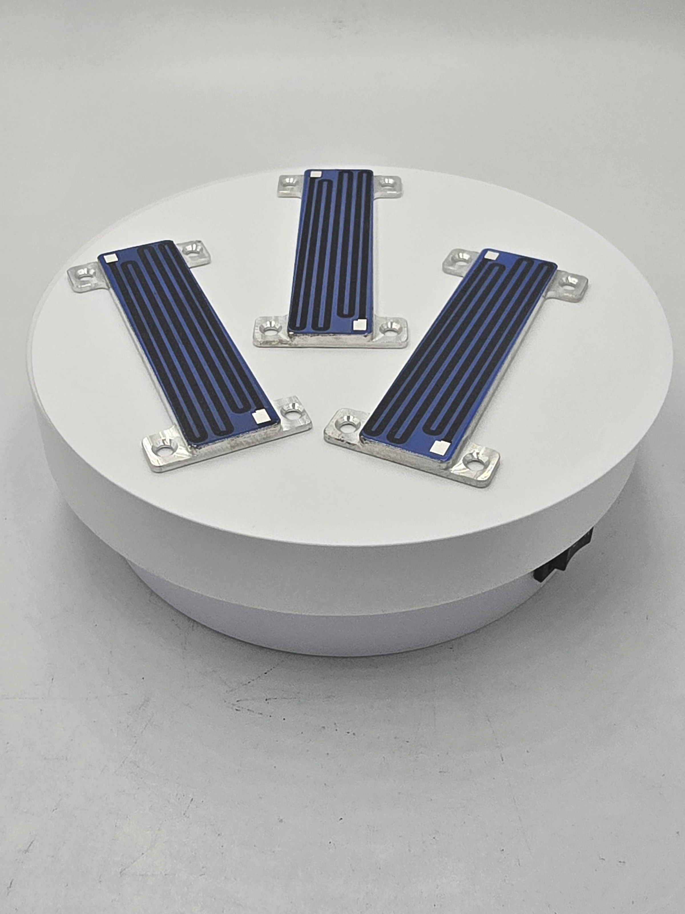 Three elongated metal-backed heater strips with blue dielectric coverage, resistive paths and end apertures.