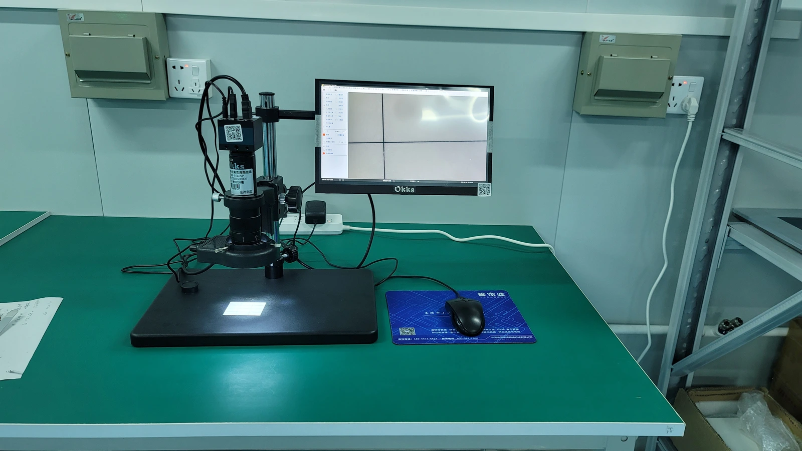 An optical inspection instrument with a specimen stage and adjacent monitor on a laboratory bench.
