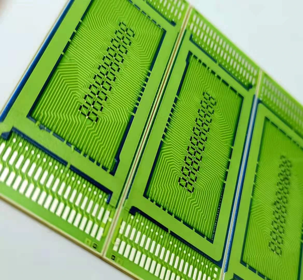 Oblique close view of a green-coated printed circuit panel with dense conductor paths and long edge contact rows.