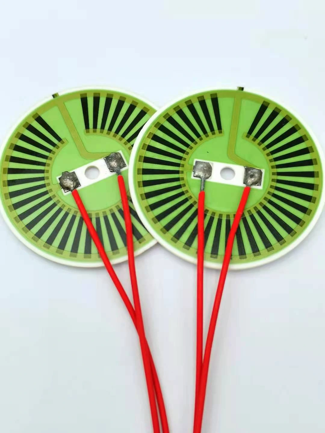 Two round heater elements with radial resistive paths, central connections and red leads.