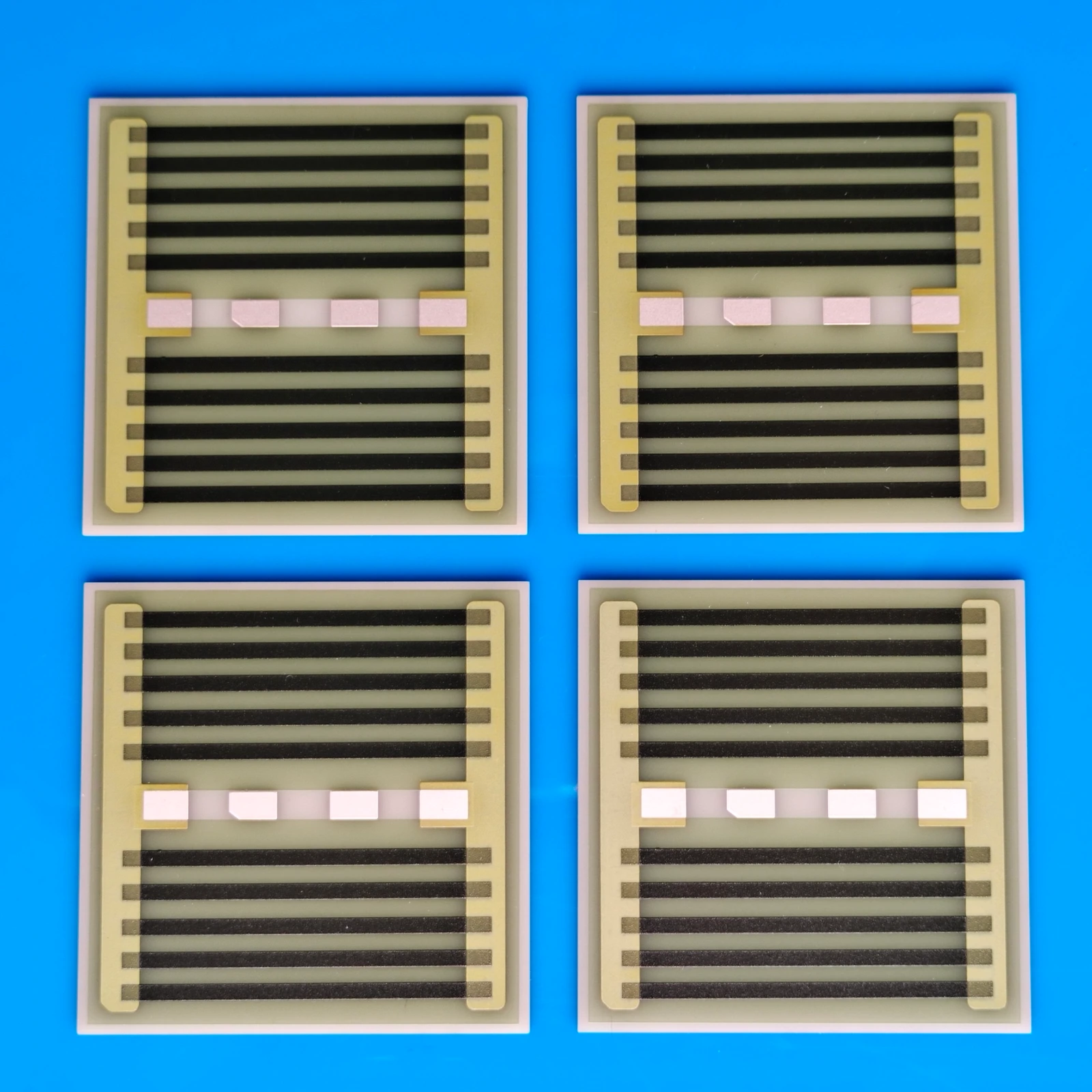Four rectangular heater patterns with parallel black resistive strips, perimeter conductors and exposed central pads.