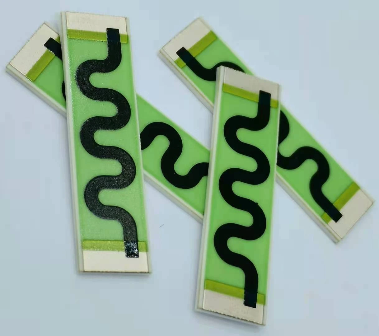 Two ceramic resistor strips with serpentine black paths, green protective coverage and exposed end terminals.