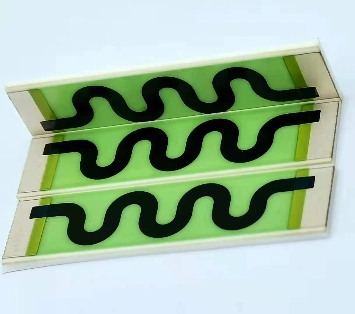 Three long serpentine resistor patterns on a ceramic panel with green protective coverage and end pads.