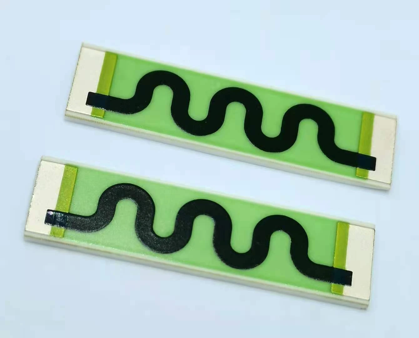 Two ceramic resistor strips showing curved black resistive paths and exposed metal end connections.