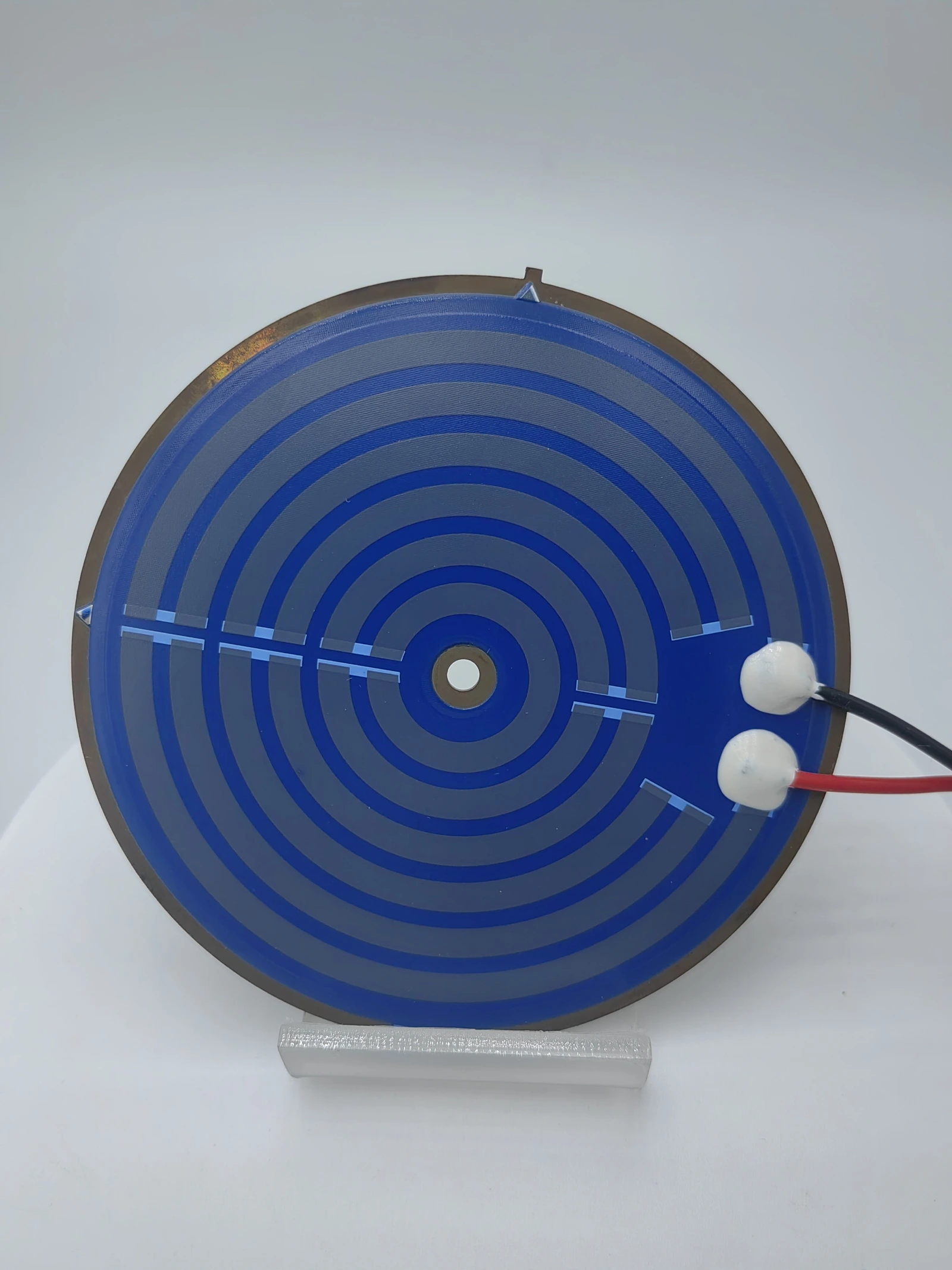 A circular blue-coated heater with spiral resistive routing and attached terminal leads.