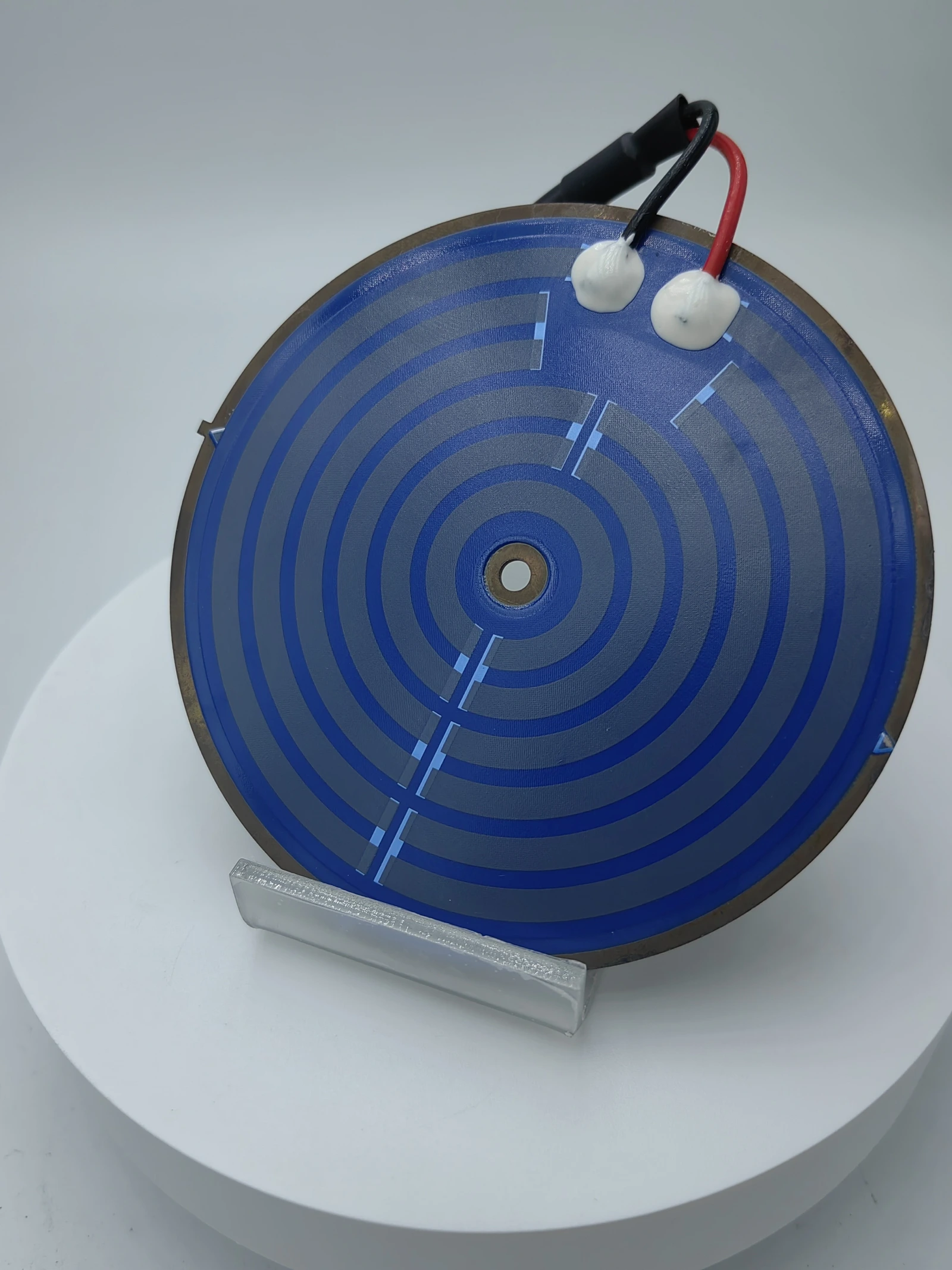 An oblique view of a blue-coated circular heater showing its spiral pattern and edge lead attachments.
