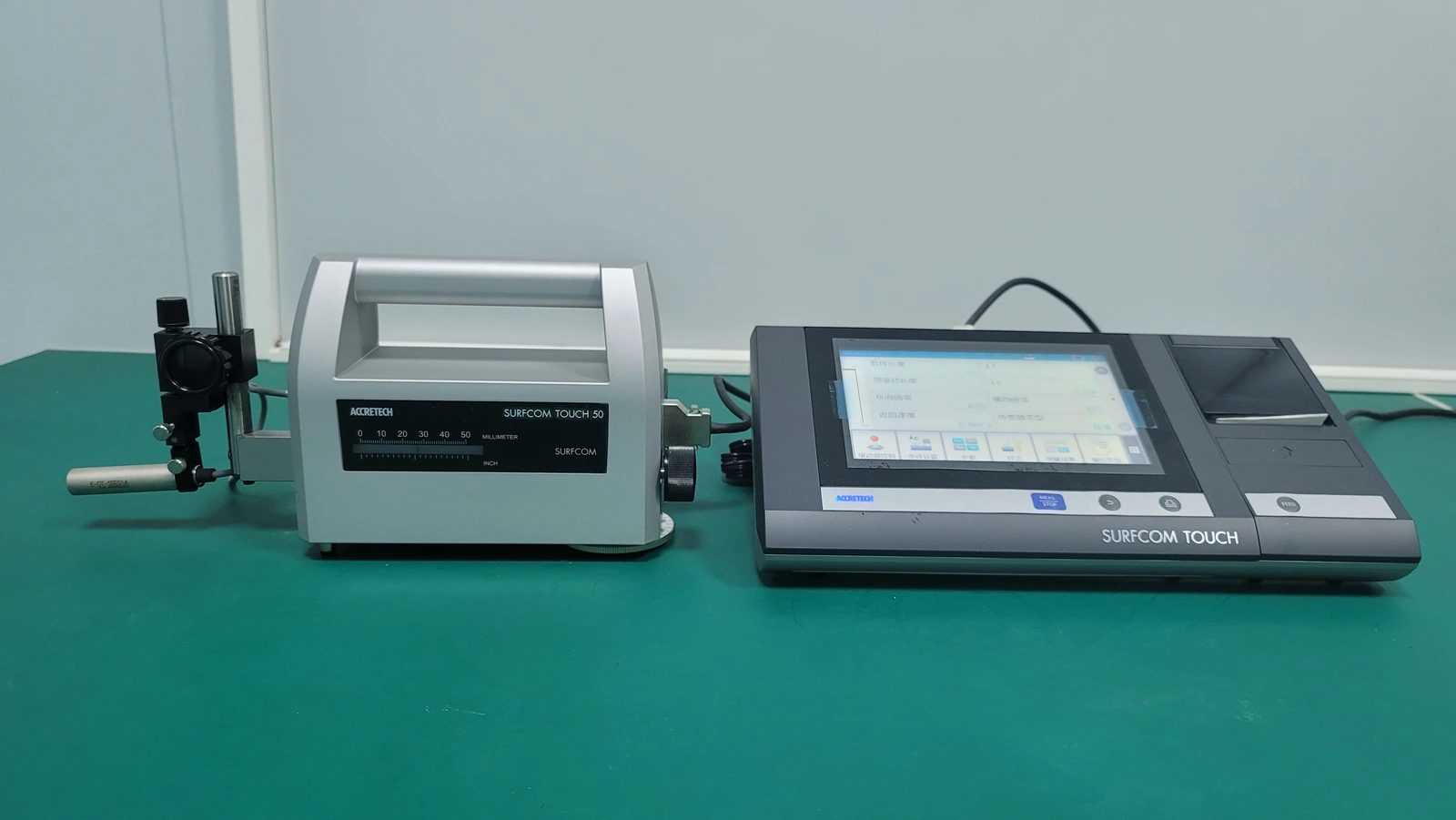 A stylus surface-profiling instrument beside its connected controller on an inspection bench.