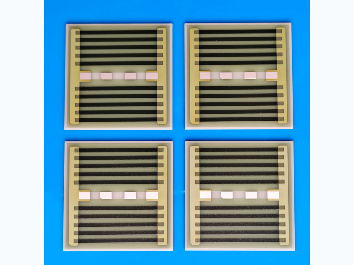 Four square AlN thick film heaters with dark serpentine resistance paths and terminal pads on a clean blue surface