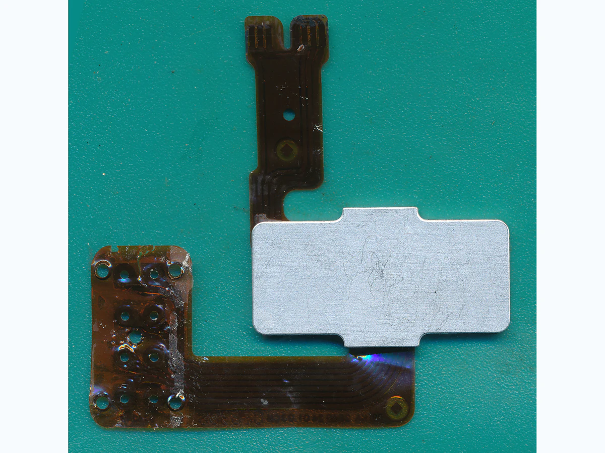 Custom polymer thick film circuit with flexible copper-colored paths, contact pads, and a metal-backed area on a clean green surface