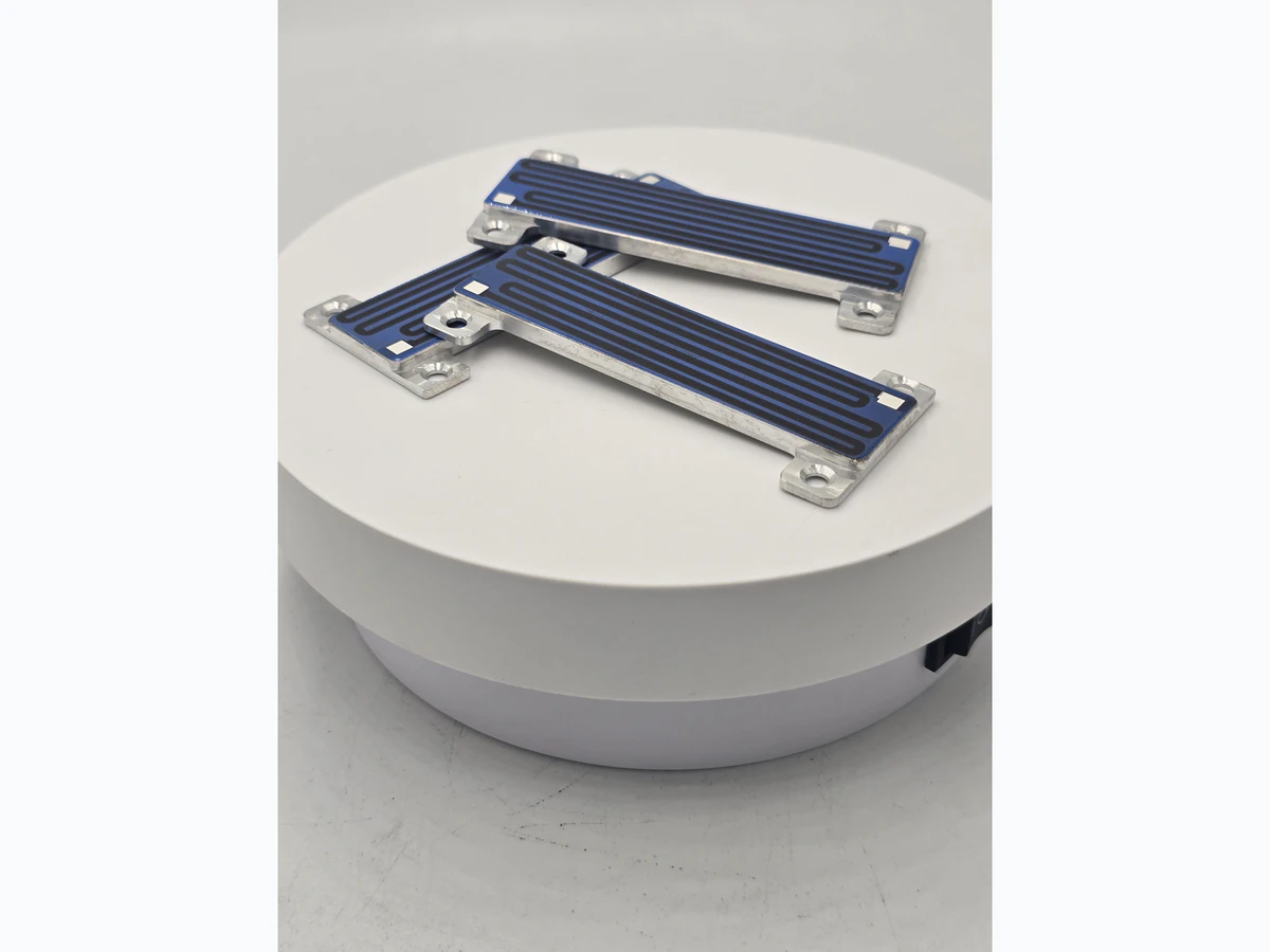 Compact heater module showing a visible serpentine path, blue field, pads, and metal support