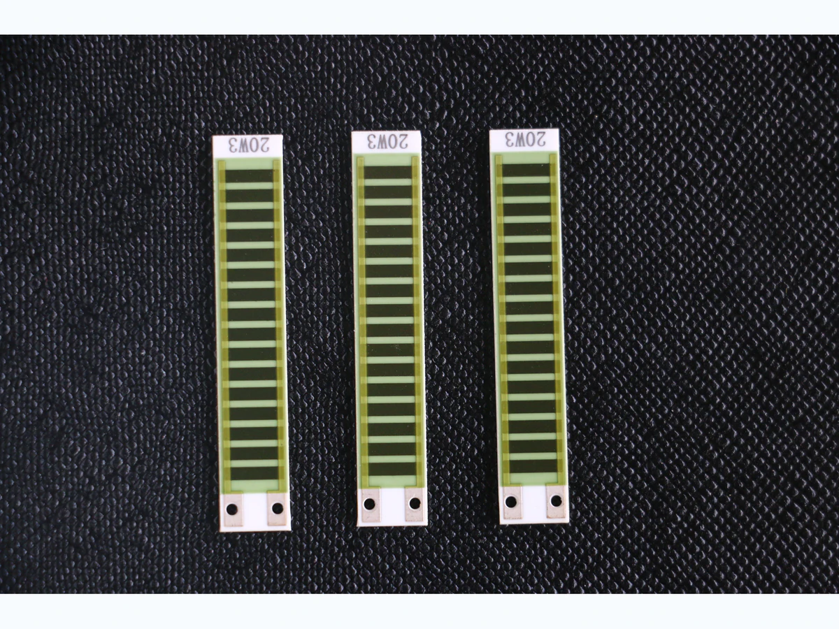 Three long ceramic thick film resistor network strips with repeated printed elements and value labels on a clean black surface