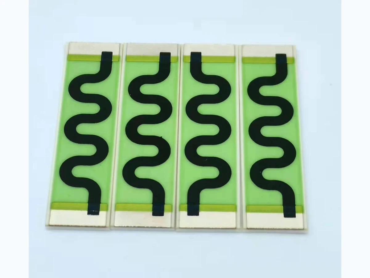Four long high voltage thick film resistors with black serpentine tracks on green ceramic strips