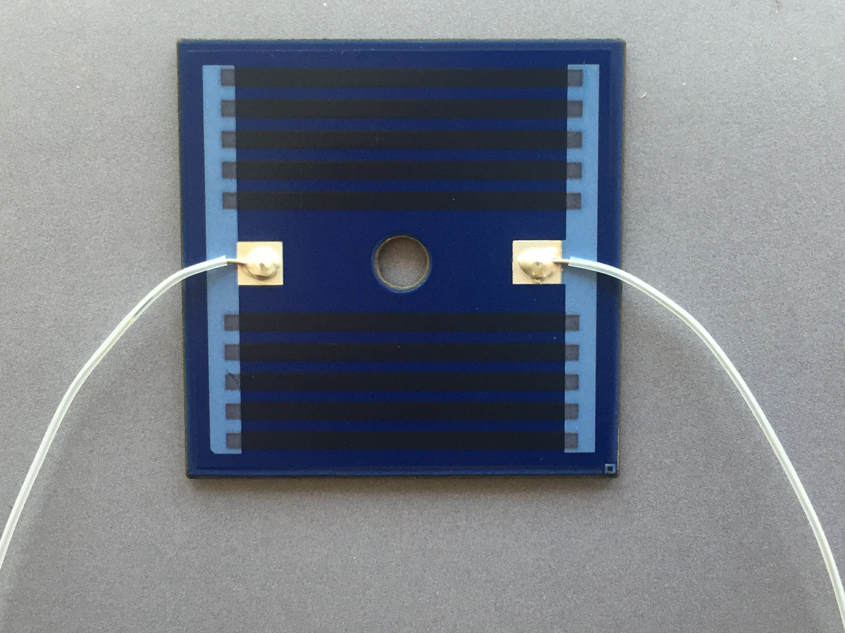 Controlled detail crop of a verified stainless steel thick film heating plate showing parallel tracks, center hole, and terminals
