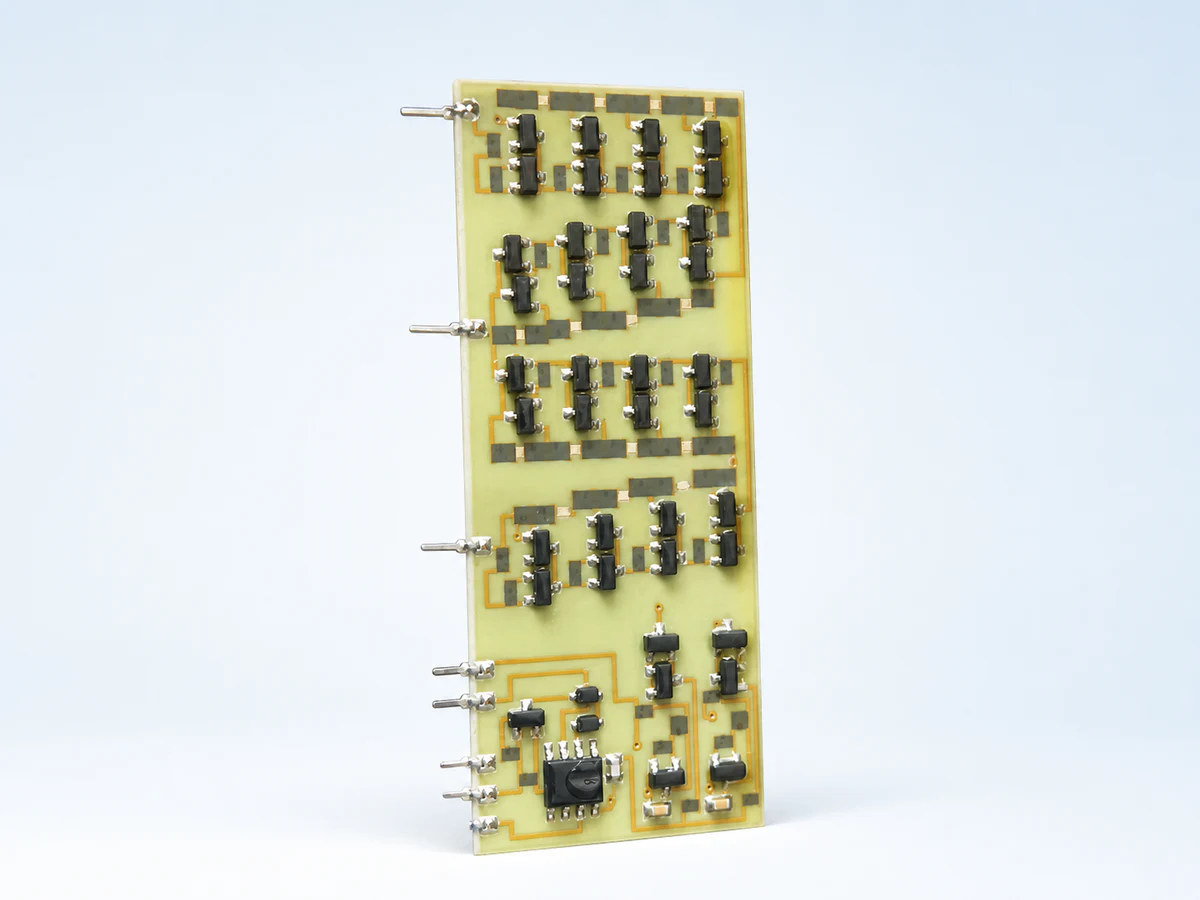 Clean studio view of a real pale-green rectangular ceramic circuit populated with black components, silver solder joints, gold conductor paths, and side terminals