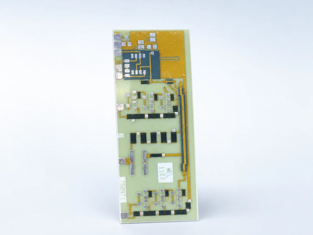 Clean studio view of a real elongated ceramic circuit with visible conductors, pads, components, terminals, and product markings