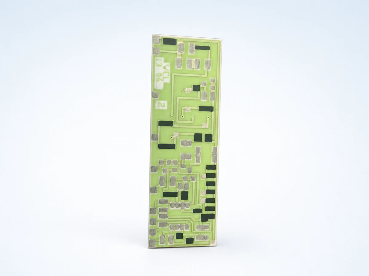 Studio product view of a pale-green ceramic circuit with silver pads, dark printed features, and visible surface routing