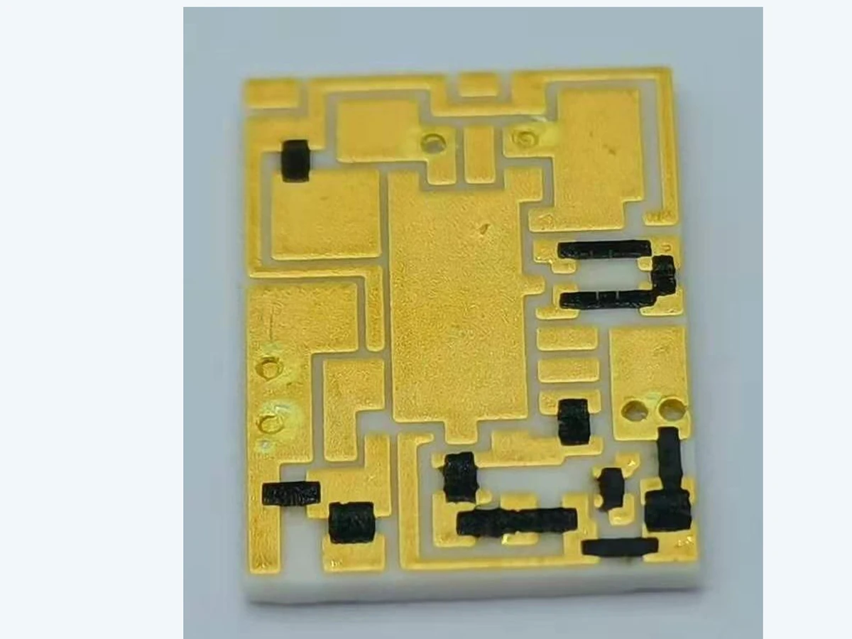 Verified close view of a thick film filter circuit showing gold-colored patterned regions and dark functional features on ceramic