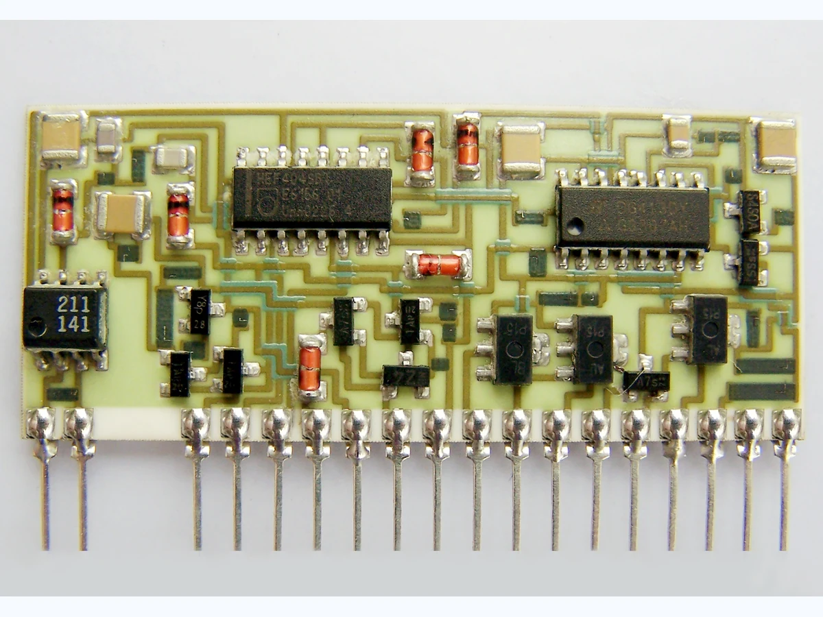 Supplied thick film hybrid circuit photograph showing printed routing, mounted components, and a row of metal leads