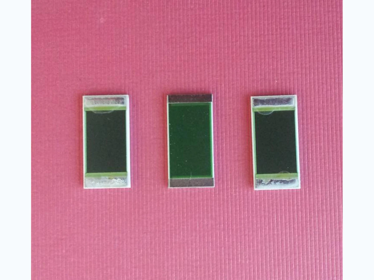 Three rectangular thick film power resistors with broad dark resistor films and silver-colored end terminals on a clean pink surface